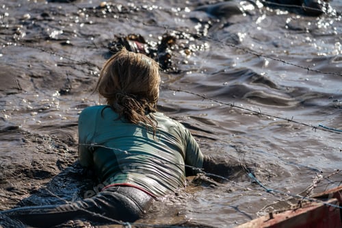 Preview: Female Athlete Crawling In Mud Under Barbed Wire At An Obstacle Course Race