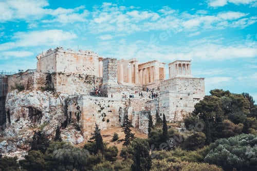 Preview: Ancient Acropolis On Tree Lined Hill Under Blue Sky With Scattered White Clouds In Greece