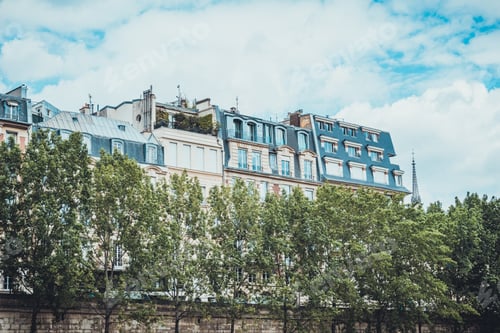 Preview: Top Sections Of Rows Of Apartment Buildings With Trees And Wall In Front Under Partly Cloudy Skies