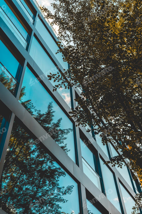 Preview: High Formated Picture Of Modern Glass Facaded Building In Darken Colors With Autum Trees On The