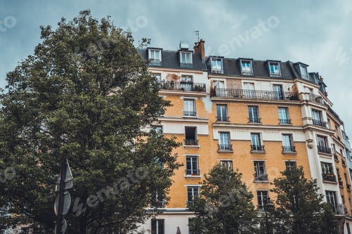 Preview: Yellow Brick Apartment Building With Dormer Windows And Single Chimney On Roof With Cloudy Skies