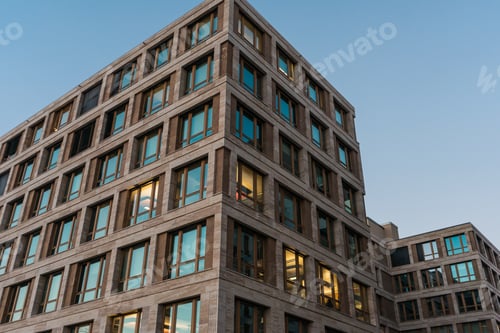 Preview: Modern Office Block At Dusk With Glowing Lights In Some Of The Windows Against A Twilight Sky