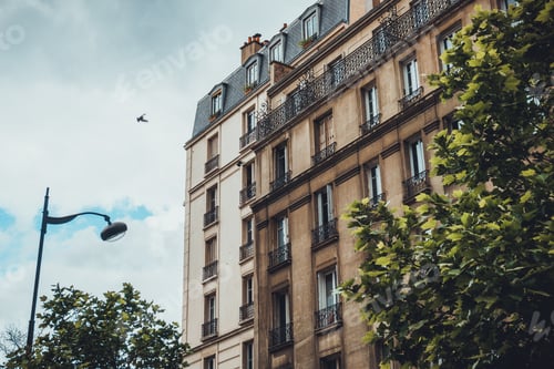 Preview: Smaller Building In Front Of Larger Apartments With Object Flying In The Sky Above Tree And Street