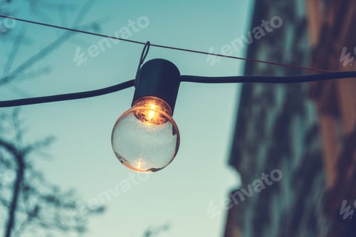 Preview: Burning Street Light With A Simple Globe And Socket Strung On A Cable In Front Of A High-Rise Urban