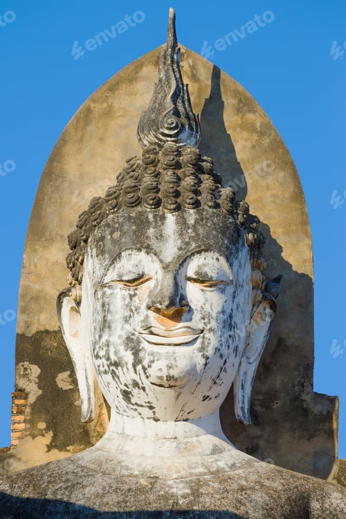 Preview: Head Of Ancient Buddha Sculpture Close-Up On A Background Of Blue Sky. Fragment Of A Buddhist
