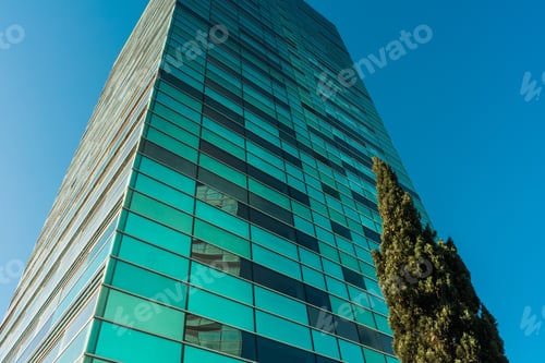 Preview: Green Skyscraper In Low Angle View With Tree On The Right Side