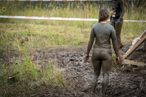 Preview: A Woman In Muddy Clothes Standing Next To An Obstacle At A Mud Run