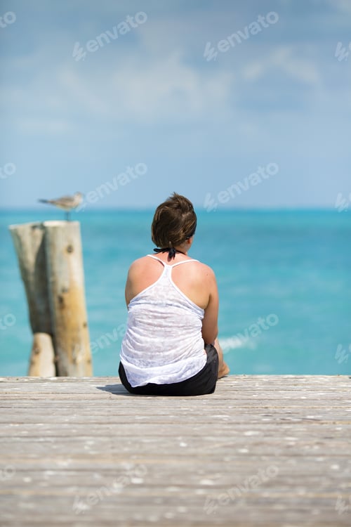 Preview: Lonely Woman Is Sitting At The End Of The Wooden Pier And Looking At The Sea. A Seagull Is Sitting