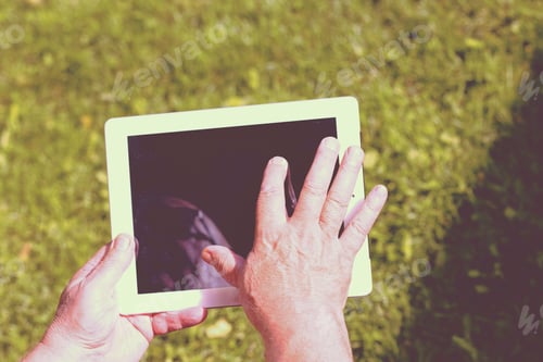 Preview: An Elderly Man Browsing The Internet With A Tablet Outdoor With A Green Grass On The Background