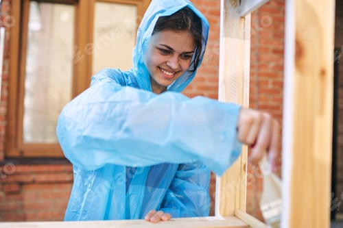 Preview: A Woman In A Raincoat Is Painting Wood In A Village