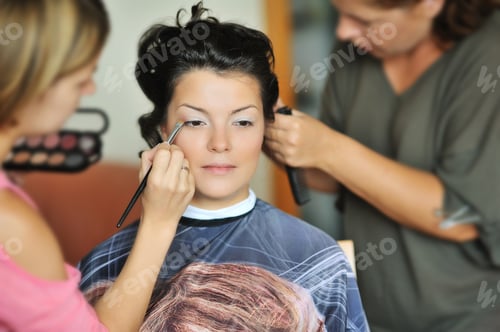 Preview: Young Beautiful Bride Applying Wedding Make-Up By Make-Up Artists
