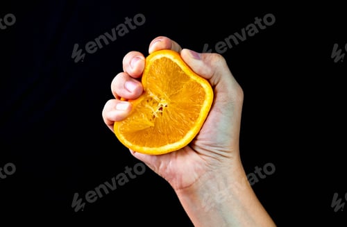 Preview: Female Hand Is Squeezing Orange Isolated On Black Background.