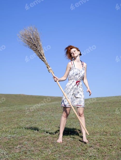 Preview: Young Red-Haired Witch At Green Grass Field With Broom.