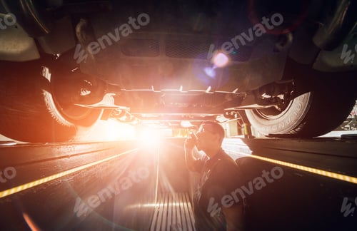 Preview: Car Mechanic Examining Car Suspension Of Lifted Automobile At Repair Service Station. Background