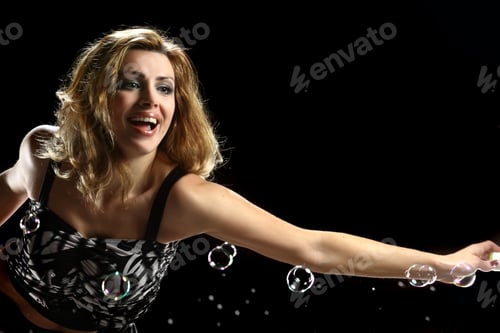 Preview: Young Beautiful Woman Blowing Soap Balls On A Black Background. Vivid Emotions. Dynamics