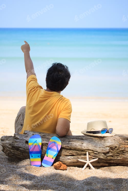 Preview: A Man Sitting On The Beach With Hat Over Old Log And Slippers
