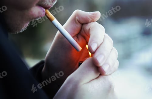 Preview: A Caucasian Man Is Lighting Up A Cigarette Outdoors. Focus Point Is On The Cigarette. Image Has A
