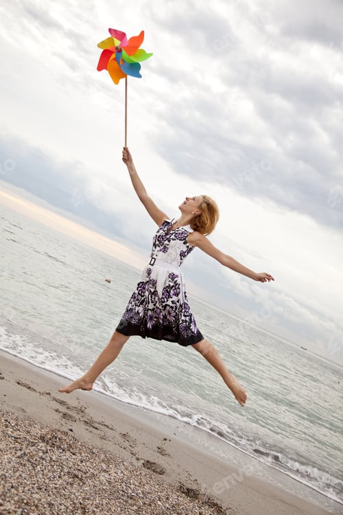 Preview: Blonde Girl Jumping With Wind Turbine At Beach.