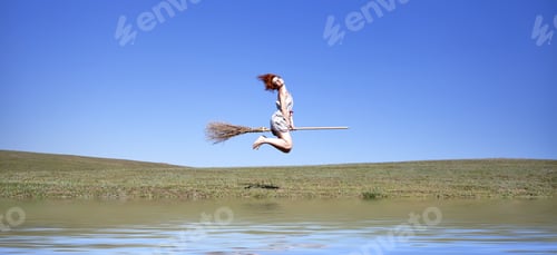 Preview: Young Red-Haired Witch On Broom Flying Over Green Grass Field And Water