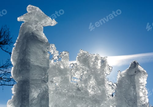 Preview: Melting Glacial Block Of Ice With Sun Behind On Blue Sky Background.