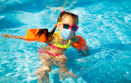 Preview: Young Toddler Girl Playing In A Water Paddling Pool Wearing A Face Mask Due To Coronavirus Outbreak