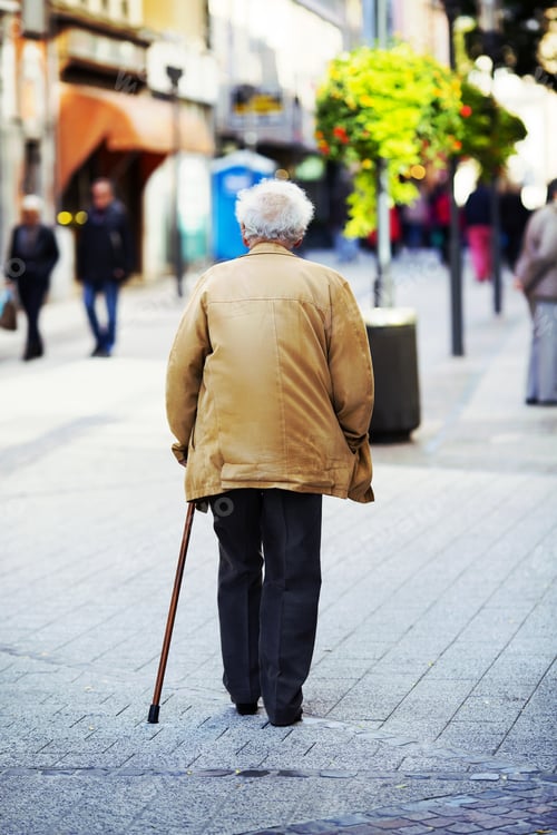 Preview: An Elderly Man Is Walking In The City With A Walking Stick. Some Unidentified Person Are Walking In