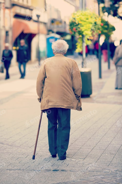 Preview: An Elderly Man Is Walking In The City With A Walking Stick. Some Unidentified Person Are Walking In