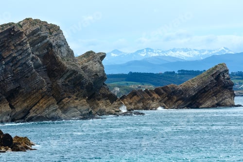 Preview: Atlantic Ocean Rocky Coastline Landscape (Spain) And Mountains With Snow In Background .