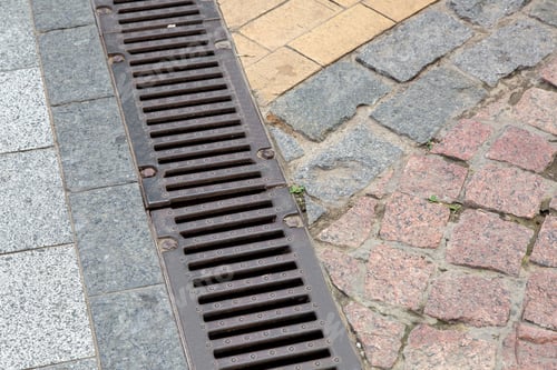 Preview: Drainage Grate Of A Storm System On A Pedestrian Sidewalk Made Of Stone Tiles, Close Up.