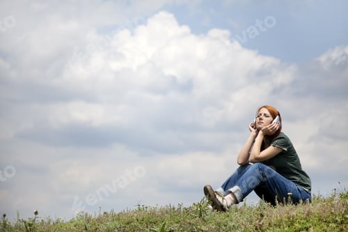 Preview: Young Smiling Girl With Headphones Sitting At Green Grass.