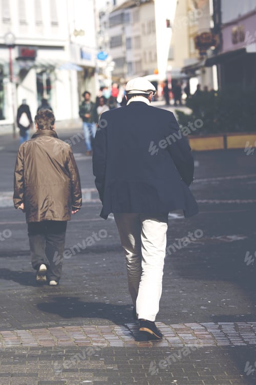 Preview: A Man Is Walking In The Streets. The Man Has A White Cap And White Trousers With Blue Jacket. Image