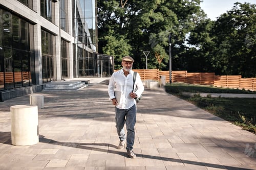 Preview: Man In Baggy Jeans And Cap Walks Outside. Stylish Adult Guy In White Shirt And Beige Cap Posing