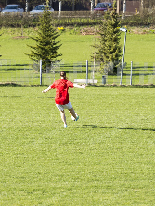 Preview: A Girl Is Kicking A Football On A Football Field On A Sunny Day. The Girl Is Wearing A Red Shirt