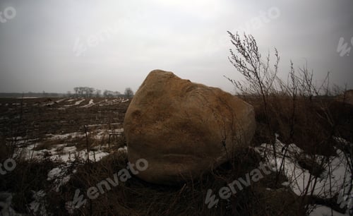 Preview: Winter Landscape With Huge Brown Stone On A Field With Dry Plants And Snow