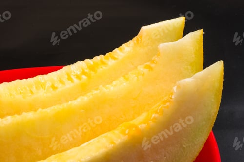 Preview: Slices Of Ripe Juicy Melon In Red Plate On Black Background