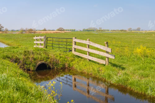 Preview: Closed Gate Reflected In The Mirror Smooth Water Surface Of A Stream Next To A Large Pasture In A