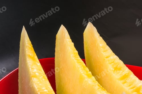 Preview: Slices Of Ripe Juicy Melon In Red Plate On Black Background