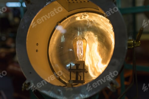 Preview: Vintage Electric Light Bulb With Incandescent Filament Inside Porthole-Shaped Projector.