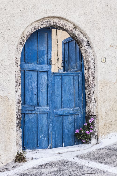 Preview: Blue Wooden Doors With Small Window And Flower At The Bottom, Santorini, Greece