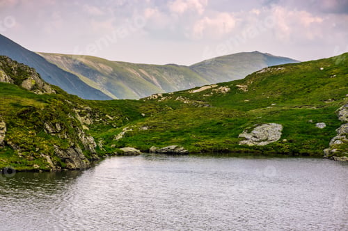 Preview: Clear Lake In Mountains With Grass On Rocky Hillside. Beautiful Mountain Ridge In Far Distance