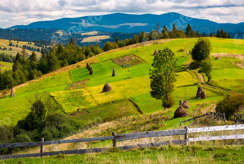 Preview: Fence In Front Of A Rural Fields On Hills. Haystack On A Grassy Slope And Mountain Ridge In The