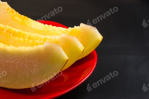 Preview: Slices Of Ripe Juicy Melon In Red Plate On Black Background