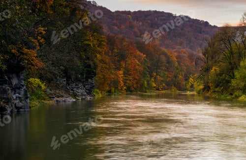 Preview: Forest River In Autumn Mountains. Lovely Grassy Shores With Yellowed Trees And Rocky Cliff