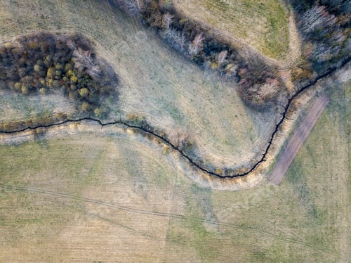 Preview: Aerial View Of Small Country River Bed Wavy In Spring Time In Countryside With Dry Grass And Some