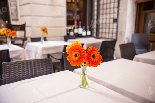 Preview: Small Bouquet Of Orange Gerberas On White Tablecloths In Cozy Italian Cafe.