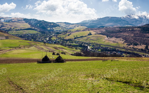Preview: Rural Area In Carpathian Mountains. Haystacks On Grassy Agricultural Fields. Village Down In The