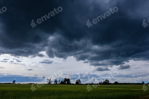 Preview: Contrast Rain Storm Clouds Over Green Meadow And Some Trees In Summer. Blue Sky Before The Rain