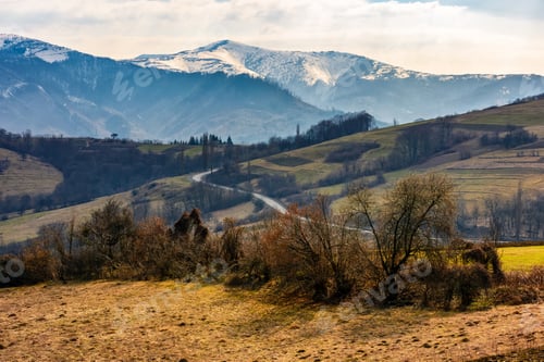 Preview: High Mountain Ridge With Snowy Peaks. Hillside With Forest In Springtime. Road Winds Through Rural
