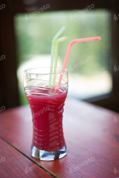 Preview: Glass With Red Juice And Colored Straws On A Table