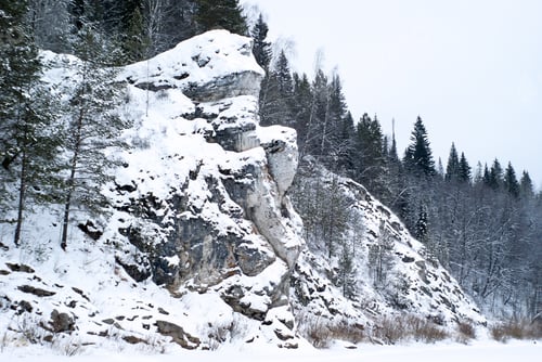 Preview: A Picturesque Rock On The Shore Of A Winter Frozen Pond In The Wooded Mountains